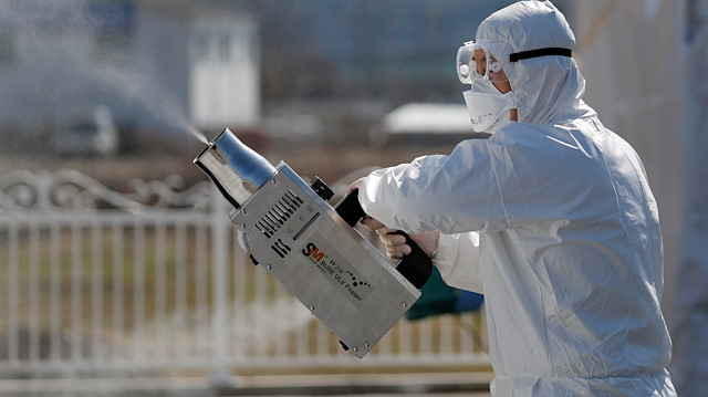A quarantine worker in protective gear sprays disinfectants at a screening facility
