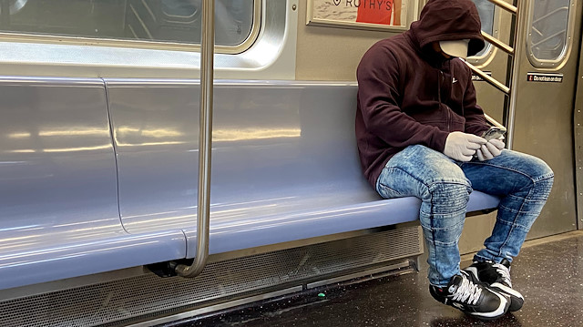A man wearing gloves to use his cell phone sits alone on a row of seats
