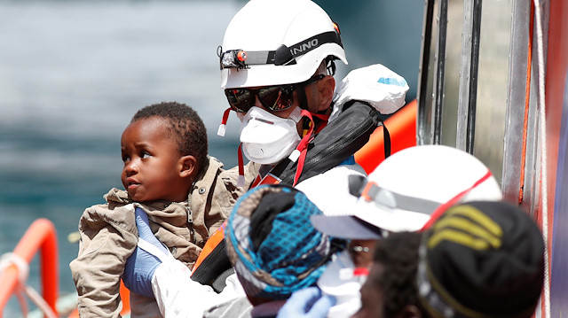 A child migrant is carried by a rescue worker as migrants wait to disembark 