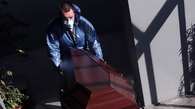 A mortuary worker in a protective suit pushes a trolley with a coffin of a person