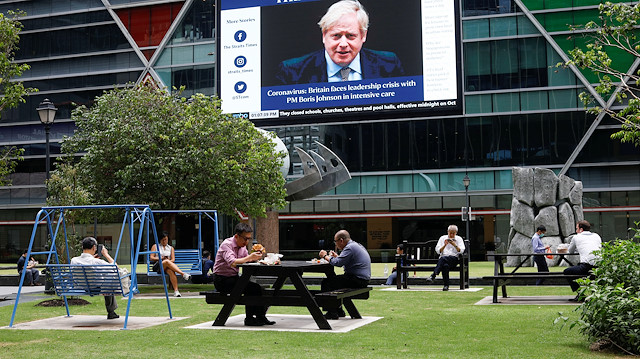 Workers take their lunch outdoors as a screen giving information about British Prime Minister
