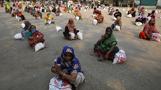 Women sit on the ground maintaining social distance waiting to receive relief supplies 