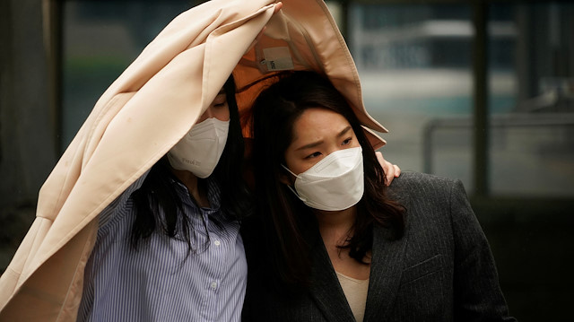 Women wearing masks to avoid the spread of the coronavirus disease (COVID-19) take cover from strong wind and rain in central Seoul, South Korea, April 20, 2020