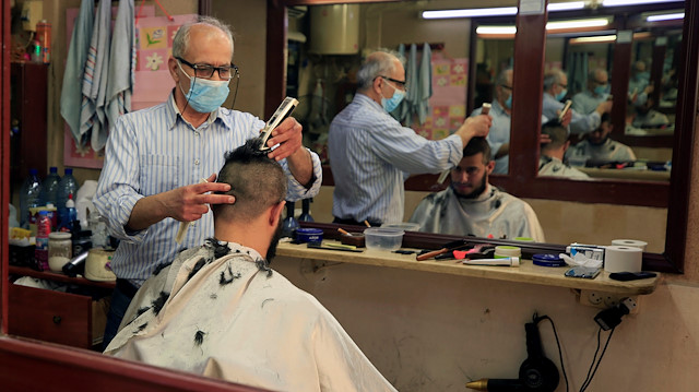 A barber wearing a protective mask shaves a customer's head at his shop
