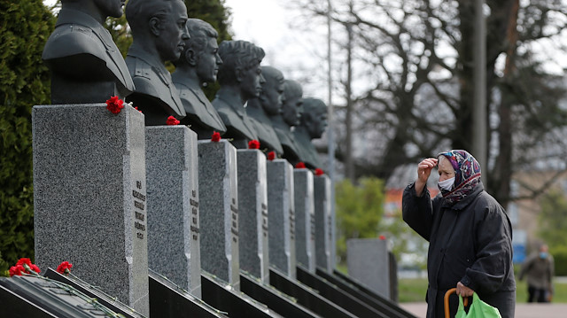 A woman wearing a protective mask prays at a memorial dedicated to firefighters