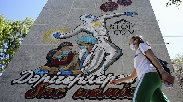 A woman wearing a protective mask walks past a mural, dedicated to medical specialists 