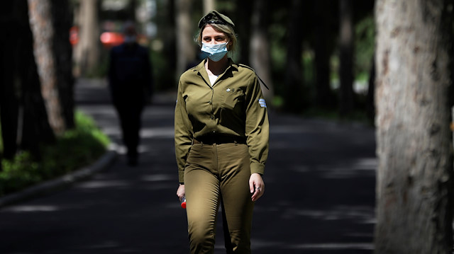 An Israeli soldier wears a face mask and walks next to graves of fallen soldiers during a ceremony ahead of Memorial Day, which commemorates those who died during conflicts, and begins on Monday night, amid coronavirus disease (COVID-19) restrictions in Jerusalem April 26, 2020. REUTERS/Ronen Zvulun

