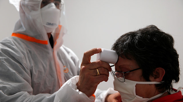 A French doctor wearing a protective suit checks the temperature of a woman 