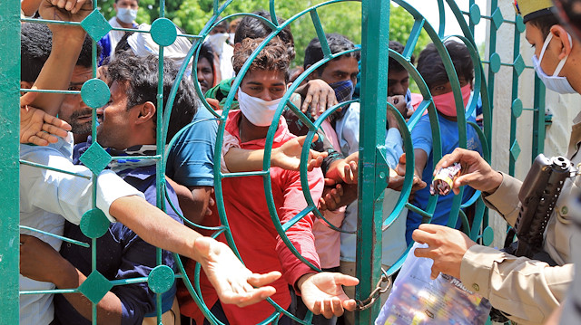 Migrant workers, who were stranded in the central state of Madhya Pradesh due to a lockdown imposed by the government to prevent the spread of coronavirus disease (COVID-19), huddle to receive biscuit packets distributed by police as they wait to leave for their home town, after they arrived in Prayagraj, India, May 1, 2020. REUTERS/Jitendra Prakash

