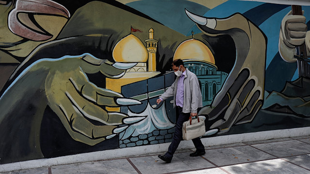 A man wearing a protective face mask walks past a Palestine mural on the wall f