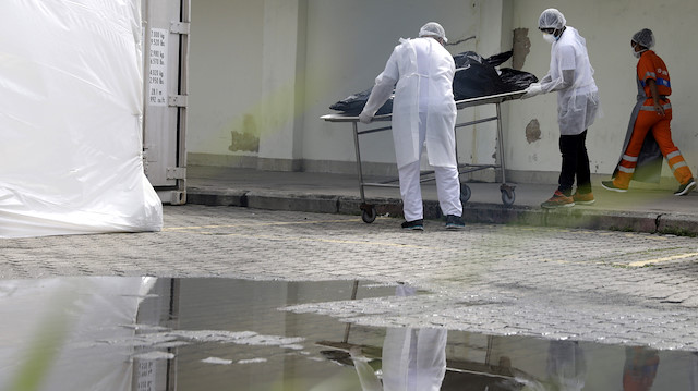 Healthcare workers wearing protective gear transport a body of a person to a refrigerated truck as they are seen reflected in a puddle during the coronavirus disease (COVID-19) outbreak, at the Lourenco Jorge hospital in Rio de Janeiro, Brazil May 8, 2020. 