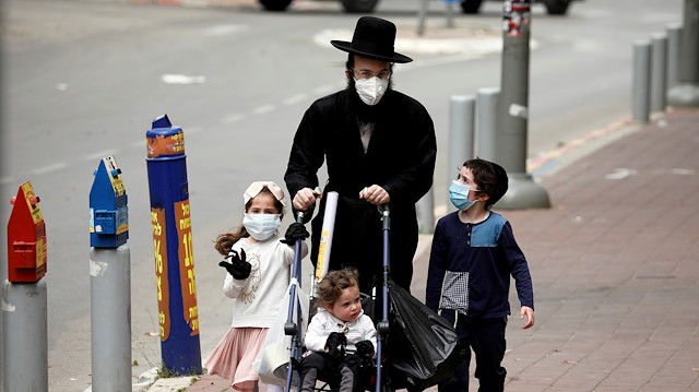 An ultra-Orthodox Jewish family wearing masks walk on a pavement 