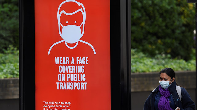 A woman wearing a protective face mask is seen at a bus stop with a public health campaign advertisement asking for passengers to wear masks on public transport, following the outbreak of the coronavirus disease (COVID-19), London, Britain, May 17, 2020. REUTERS/Toby Melville

