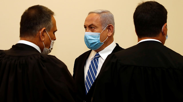 Israeli Prime Minister Benjamin Netanyahu, wearing a face mask, stands inside the court room as his corruption trial opens at the Jerusalem 