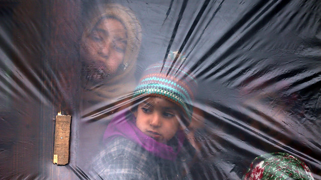 Children look out from a window, covered with a plastic sheet