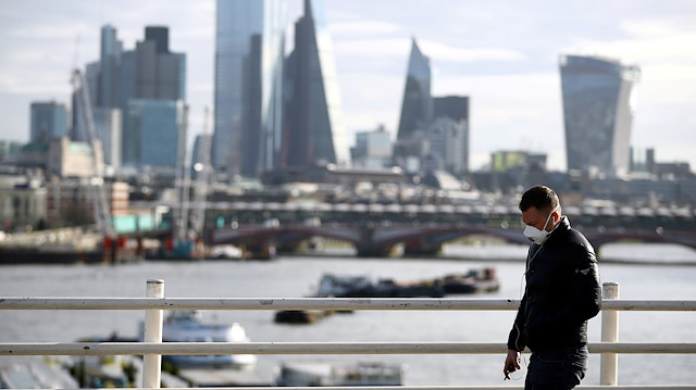 FILE PHOTO: A man wearing a protective mask walks across Waterloo Bridge in front of the City of London financial district during rush hour, as the number of Coronavirus cases grow around the world, in London, Britain, March 17, 2020.