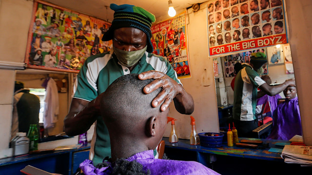 A barber wears a mask while shaving his client inside a barbershop named Old Trafford