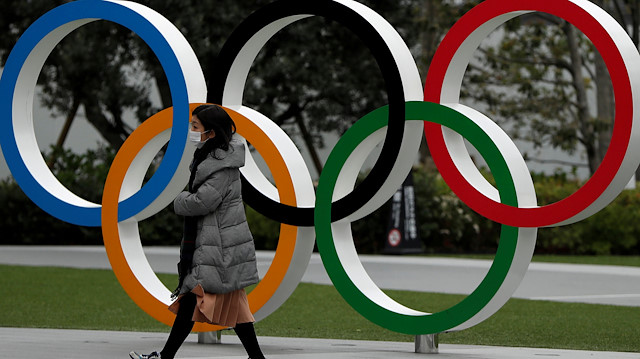 FILE PHOTO: A woman wearing a protective face mask, following an outbreak of the coronavirus disease (COVID-19), walks past the Olympic rings in front of the Japan Olympics Museum, in Tokyo, Japan March 30, 2020