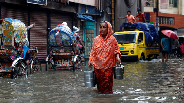 A woman carries tiffin carriers as she walks through a water-logged street after heavy rain in Dhaka, Bangladesh, July 21, 2020.