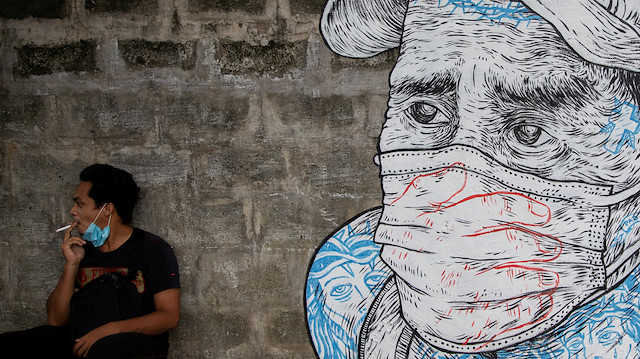 A man smokes a cigarette next to a mural of a man wearing a protective mask amid the coronavirus disease (COVID-19) outbreak in Quezon City, Metro Manila, Philippines, July 30, 2020. REUTERS/Eloisa Lopez TPX IMAGES OF THE DAY

