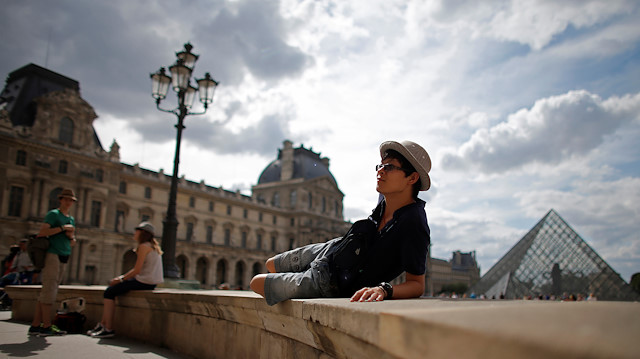 A tourist sits in front of the Pyramid at the Louvre museum in Paris, August 6, 2013.