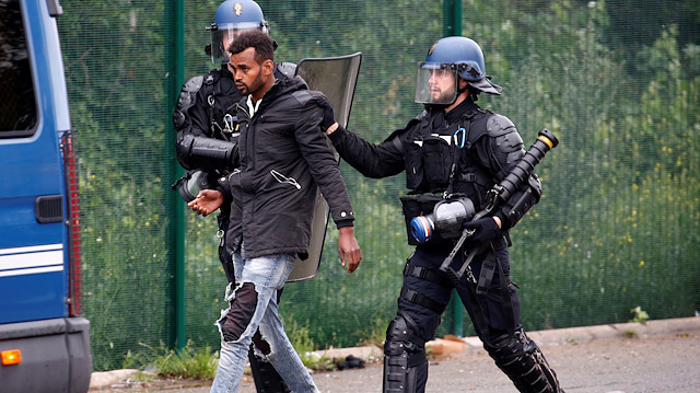 French police officers detain a migrant during the dismantling of a makeshift shelter camp 