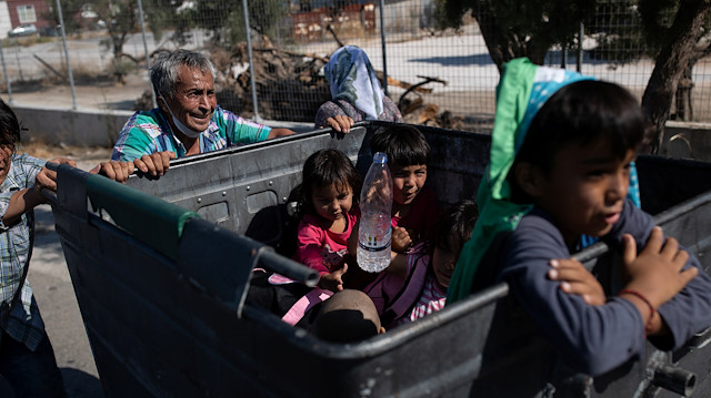 Two men push a garbage bin with their belongings as children sit inside the bin, following a fire at the Moria camp for refugees and migrants on the island of Lesbos, Greece, September 11, 2020