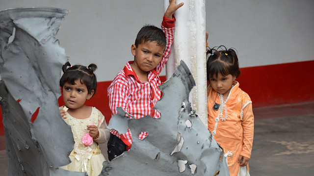 Children hold a piece of the roof of their house, damaged during recent clashes 