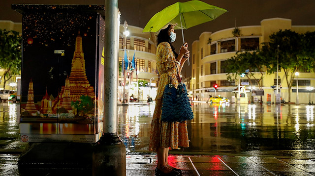 A woman wearing a mask as a protection against the coronavirus disease (COVID-19) waits to cross the street during a rainy night at Ratchadamnoen Avenue in Bangkok, Thailand, August 22, 2020.