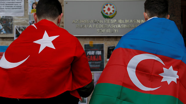 Men holding national flags of Azerbaijan and Turkey stand next to a makeshift memorial 