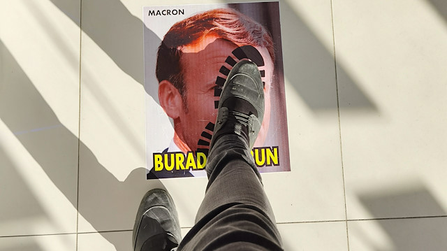 Macron'un fotoğrafının yer aldığı görselde, yüzünün üzerinde ayak izi bulunuyor ve 'Burada durun!' yazıyor.