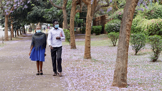A man and woman wear face masks as they walk past Jacaranda trees 