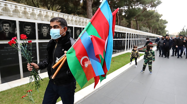 A man carries national flags and flowers as people celebrate the entry of the Azerbaijan army 