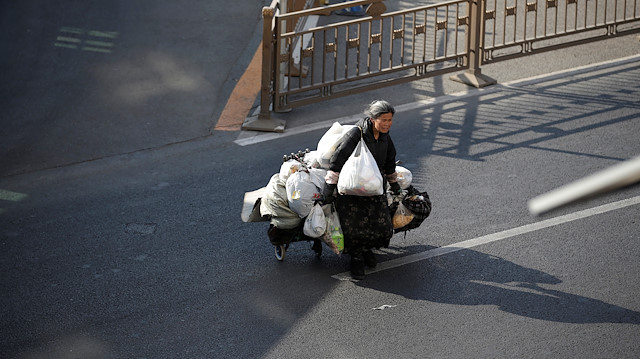 A homeless woman carrying bags crosses a road in Beijing