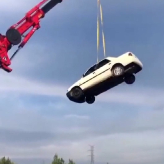 Metrelerce yükseklikteki vince bağlanan otomobilde canlarını tehlikeye attılar