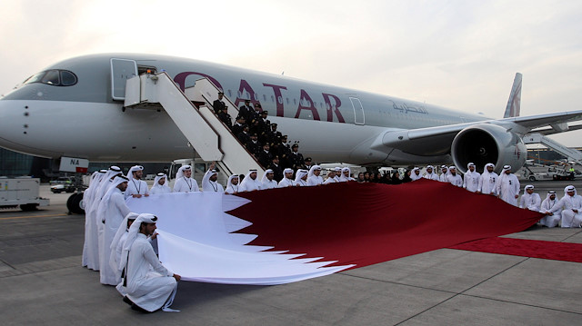 Qatar Airways staff hold a Qatari flag in front of an Airbus A350-1000 