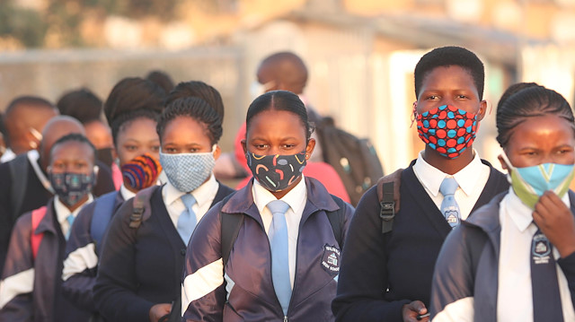 A teacher distributes masks to students as schools begin to reopen