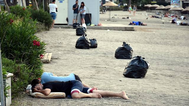 Belediye ekipleri, sahilde uyuyan tatilcilerin arasında torbalar dolusu çöp topladı.
