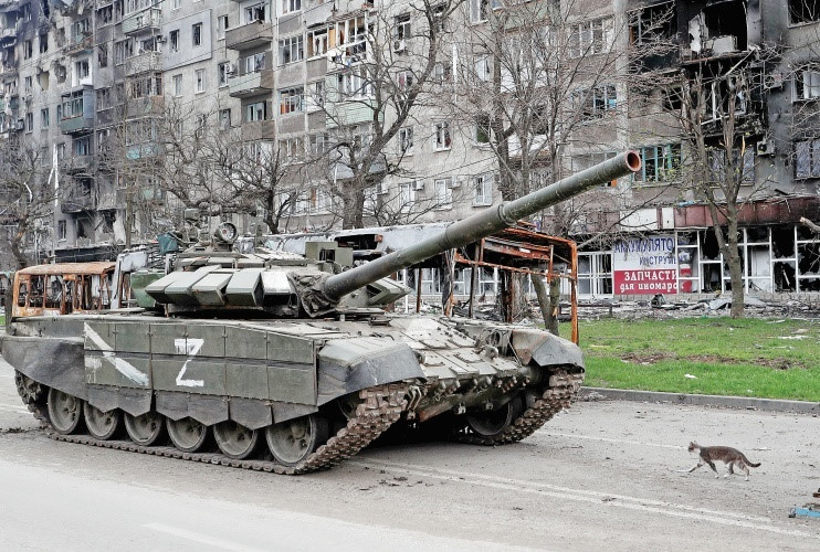 Mariupol’da savaş sırasında nağır hasar gören bir napartmanın önünde Rus nkuvetlerine ait bir tankın nyanında bir kedi yürüyor.n
