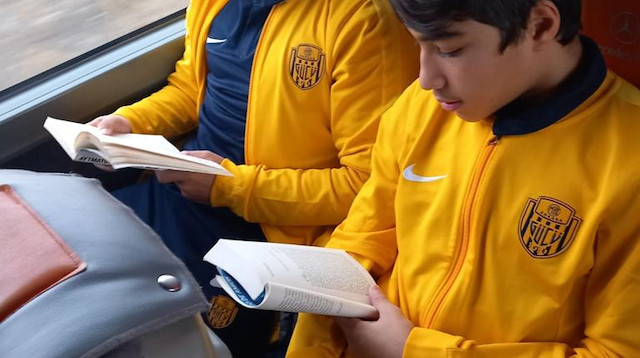 Genç futbolcular deplasman yolculuğunu kitap okuyarak değerlendiriyor. 