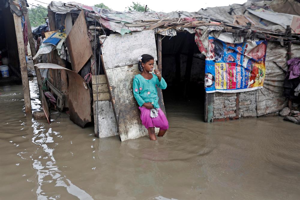 A girl brushes her teeth as she stands outside her submerged shanty
