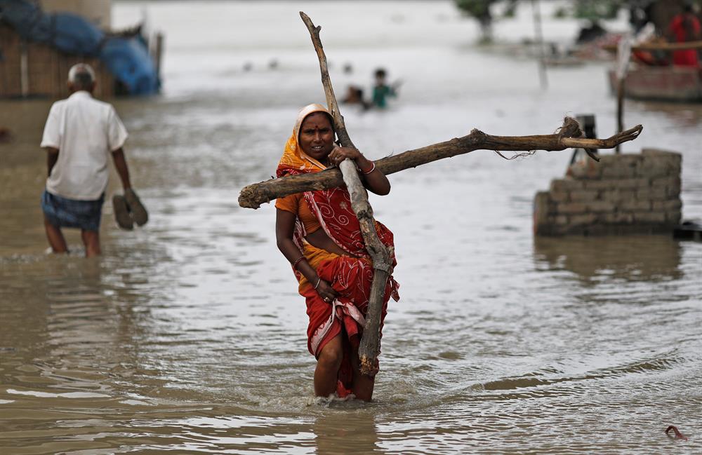 A woman wades through a flooded street carrying logs of wood to be used to reinforce her shanty