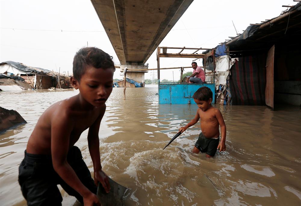 Children wade through flood waters as a man sits outside his submerged shanty